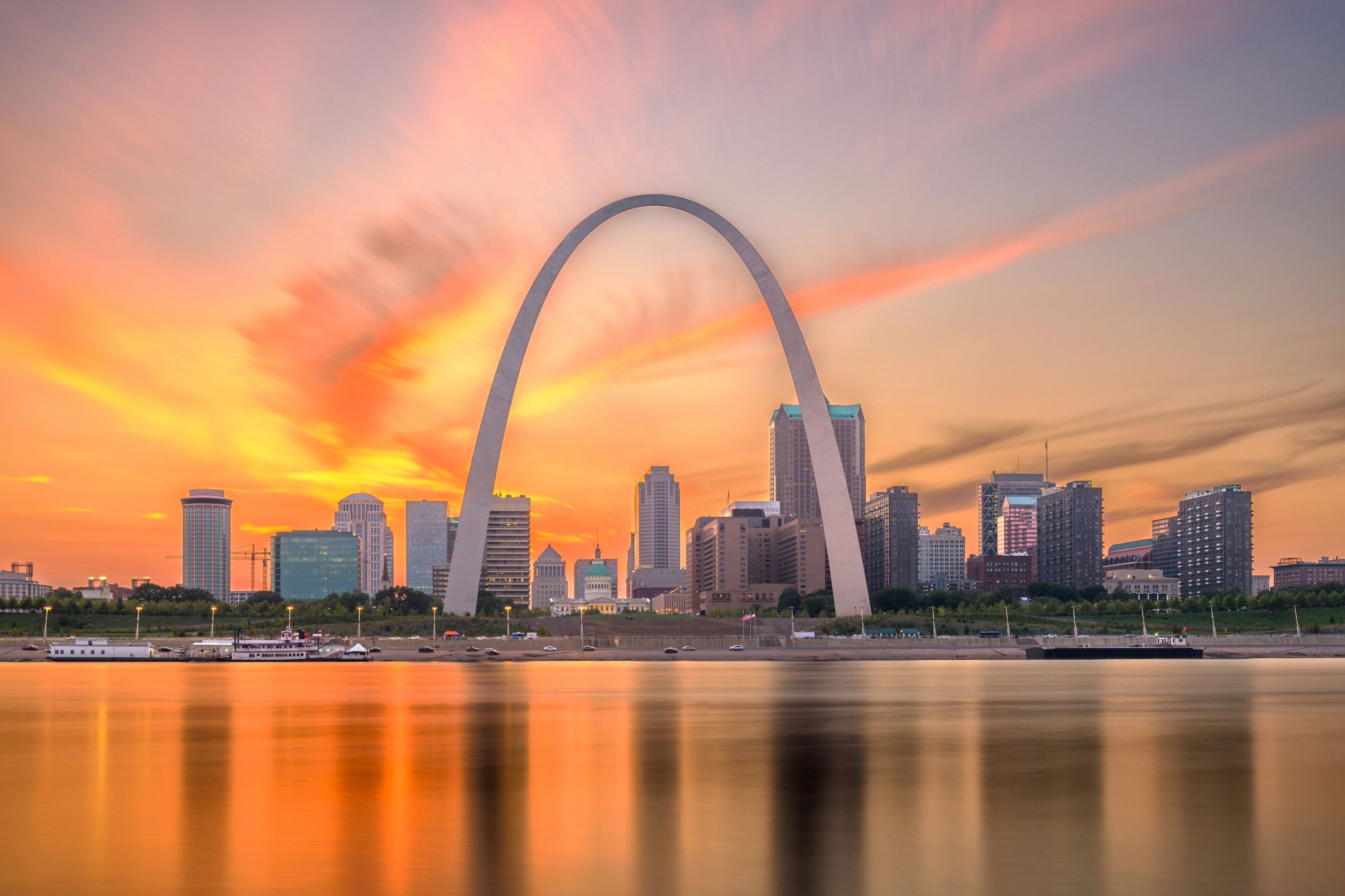 Gateway Arch in Missouri with sunset behind it and the Mississippi river in front